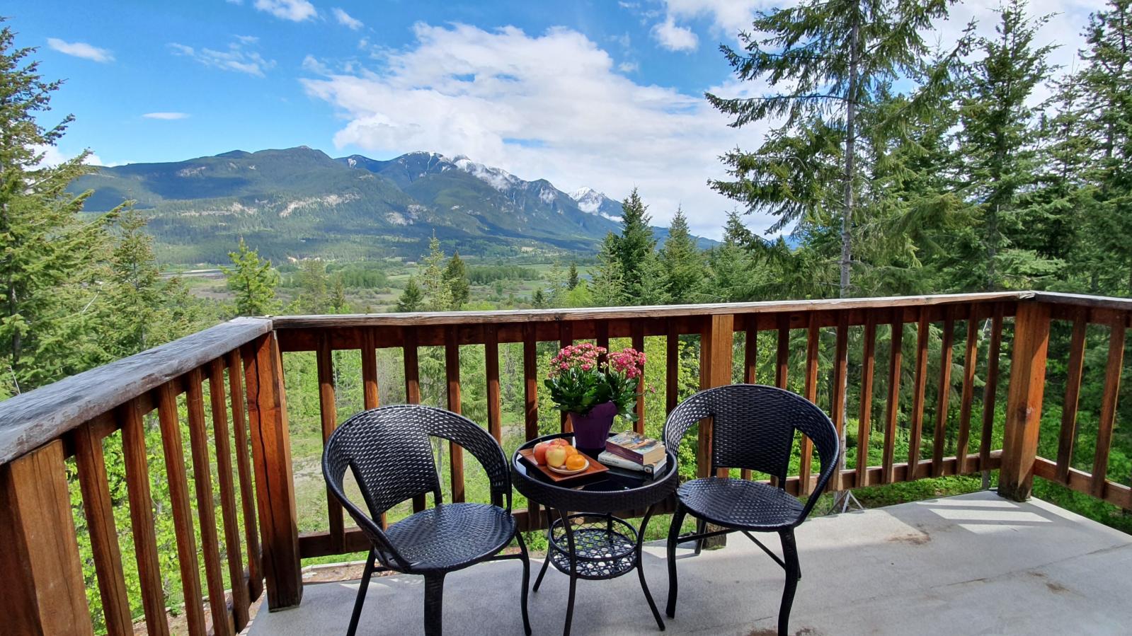 A balcony with two chairs and cafe table and summer mountain view through green pine trees. 